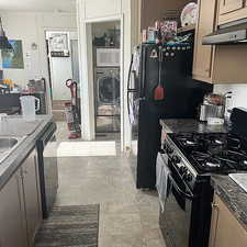 Kitchen featuring stainless steel appliances, washer / dryer, under cabinet range hood, and dark countertops