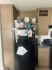 Kitchen featuring freestanding refrigerator, a textured ceiling, dark countertops, cream cabinetry, and electric stove