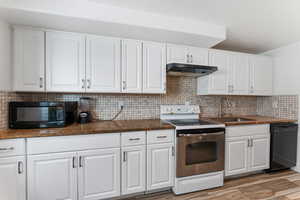 Kitchen featuring black appliances, white cabinetry, backsplash, and dark stone countertops