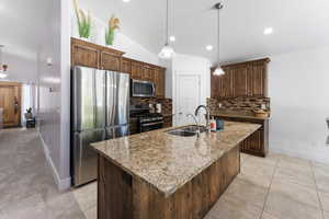 Kitchen featuring appliances with stainless steel finishes, hanging light fixtures, vaulted ceiling, light stone countertops, and decorative backsplash