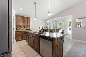 Kitchen featuring appliances with stainless steel finishes, decorative backsplash, lofted ceiling, light stone counters, and decorative light fixtures