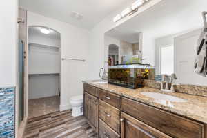 Full bathroom featuring a spacious closet, double vanity, wood finish floors, and a shower stall