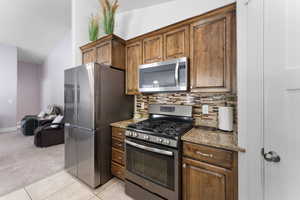 Kitchen featuring stainless steel appliances, light stone countertops, tasteful backsplash, light tile patterned floors, and lofted ceiling
