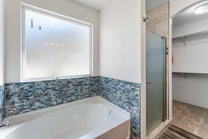 Full bath featuring a stall shower, a walk in closet, a bath, and tile walls