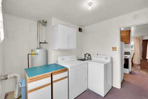 Laundry room featuring cabinet space, light carpet, water heater, and washing machine and clothes dryer