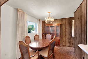 Dining space featuring wooden walls, a chandelier, and a textured ceiling
