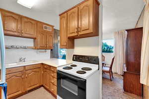 Kitchen featuring white electric range, light countertops, brown cabinets, a textured ceiling, and freestanding refrigerator