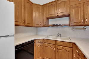 Kitchen with freestanding refrigerator, dishwasher, light countertops, and brown cabinets