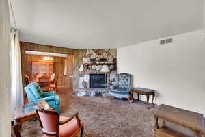 Living area featuring a stone fireplace, wood walls, a chandelier, and carpet floors