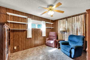 Sitting room featuring wooden walls, a textured ceiling, a ceiling fan, and carpet