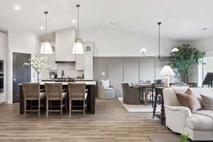 Builders Model for example purposes only. Kitchen featuring open floor plan, white cabinets, a center island with sink, backsplash, and high vaulted ceiling