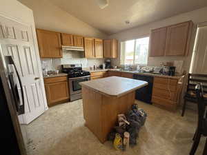 Kitchen with lofted ceiling, appliances with stainless steel finishes, a center island, brown cabinets, and light countertops