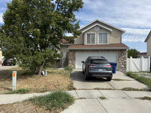 Traditional-style house with stucco siding, an attached garage, driveway, stairs, and stone siding
