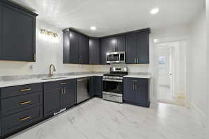 Kitchen with appliances with stainless steel finishes, light marble finish flooring, light stone countertops, and recessed lighting