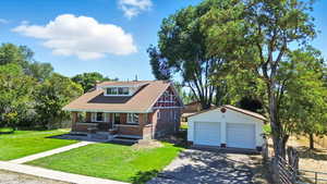 View of front facade with a detached garage, an outbuilding, brick siding, a shingled roof, and a chimney