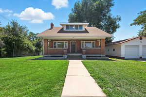 Bungalow-style house with covered porch, a front lawn, a chimney, roof with shingles, and brick siding