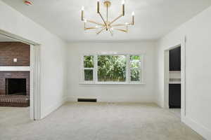 Unfurnished living room with light colored carpet, a fireplace, and a chandelier