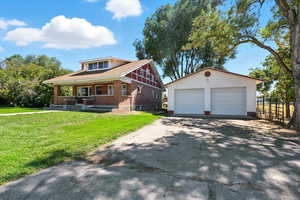 View of front facade featuring covered porch, a garage, an outdoor structure, and a front yard