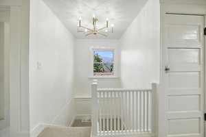 Staircase featuring a textured ceiling, carpet flooring, a chandelier, and a decorative wall