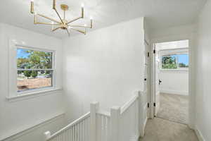 Hall featuring an upstairs landing, a textured ceiling, light carpet, and a chandelier
