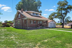 View of front of property featuring covered porch, brick siding, a chimney, a garage, and driveway
