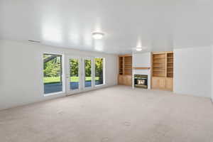 Unfurnished living room featuring light colored carpet, a fireplace, and built in shelves