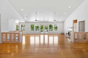 Unfurnished living room featuring high vaulted ceiling, plenty of natural light, a fireplace with flush hearth, light wood-style flooring, and recessed lighting
