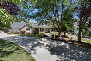 View of front facade featuring a porch, roof with shingles, stone siding, and a front lawn