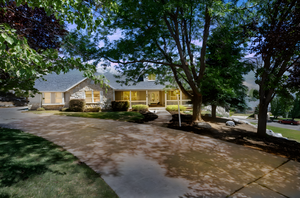 View of front of home with a porch, stone siding, concrete driveway, and a shingled roof