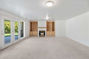 Unfurnished living room with built in shelves, a glass covered fireplace, and light carpet