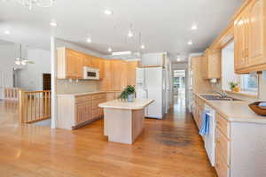 Kitchen with light countertops, light brown cabinetry, a center island, white appliances, and light wood-style floors