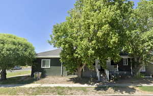 View of property hidden behind natural elements with covered porch, brick siding, and a shingled roof