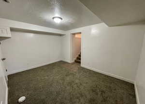 Finished below grade area with a textured ceiling, dark carpet, and stairway