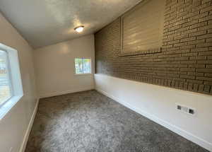 Carpeted empty room featuring a textured ceiling, lofted ceiling, and brick wall