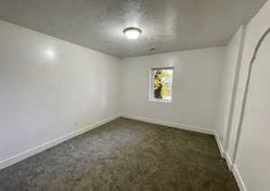 Unfurnished room featuring dark colored carpet, a textured ceiling, and arched walkways