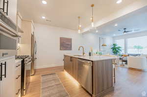 Kitchen with light brown cabinetry, light wood finished floors, pendant lighting, appliances with stainless steel finishes, and light stone counters