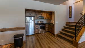 Galley Kitchen featuring dark countertops, stainless steel appliances, dark wood-style floors, and brown cabinetry