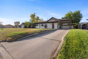 Ranch-style home with a front yard, driveway, an attached carport, and brick siding