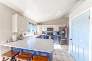 Kitchen with a kitchen breakfast bar, stainless steel appliances, a peninsula, lofted ceiling, and light tile patterned flooring