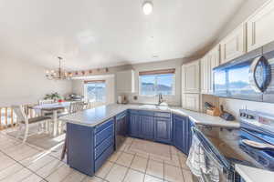 Kitchen featuring appliances with stainless steel finishes, a peninsula, decorative light fixtures, blue cabinets, and light countertops