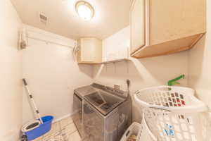 Laundry room featuring cabinet space, light tile patterned floors, a textured ceiling, and separate washer and dryer