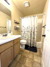 Full bathroom with a textured ceiling, shower / tub combo, vanity, and dark tile patterned floors