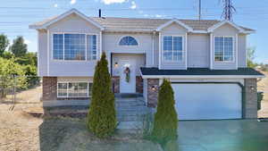 Raised ranch featuring brick siding, concrete driveway, a garage, and roof with shingles