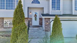 View of exterior entry with brick siding, a garage, and roof with shingles