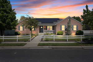 View of front of property with roof mounted solar panels, a porch, brick siding, a fenced front yard, and a shingled roof