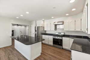 Kitchen featuring newer stainless steel appliances, white cabinetry, dark granite countertops, gas stove, and bar seating