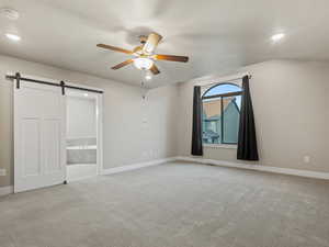 Unfurnished bedroom featuring light colored carpet, a barn door, recessed lighting, ensuite bath, and ceiling fan