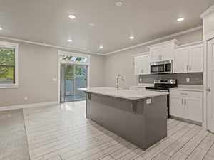 Kitchen with recessed lighting, appliances with stainless steel finishes, crown molding, white cabinets, and backsplash