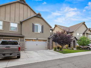 View of front facade featuring stone siding, an attached garage, driveway, and stucco siding