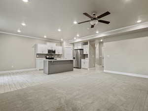 Kitchen featuring open floor plan, tasteful backsplash, light countertops, white cabinetry, and a center island with sink